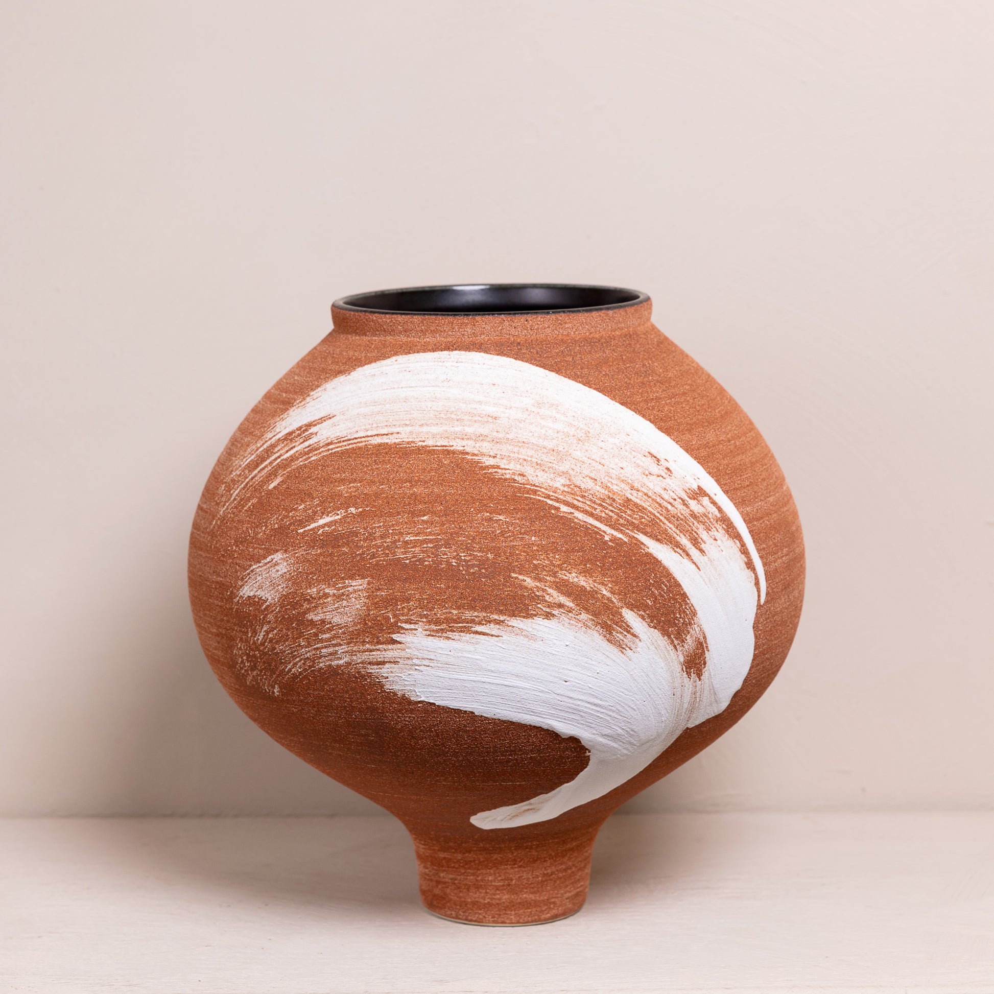 Handgemaakte aardewerk vaas met unieke witte penseelstreek op een terracotta basis, modern en rustiek ontwerp.