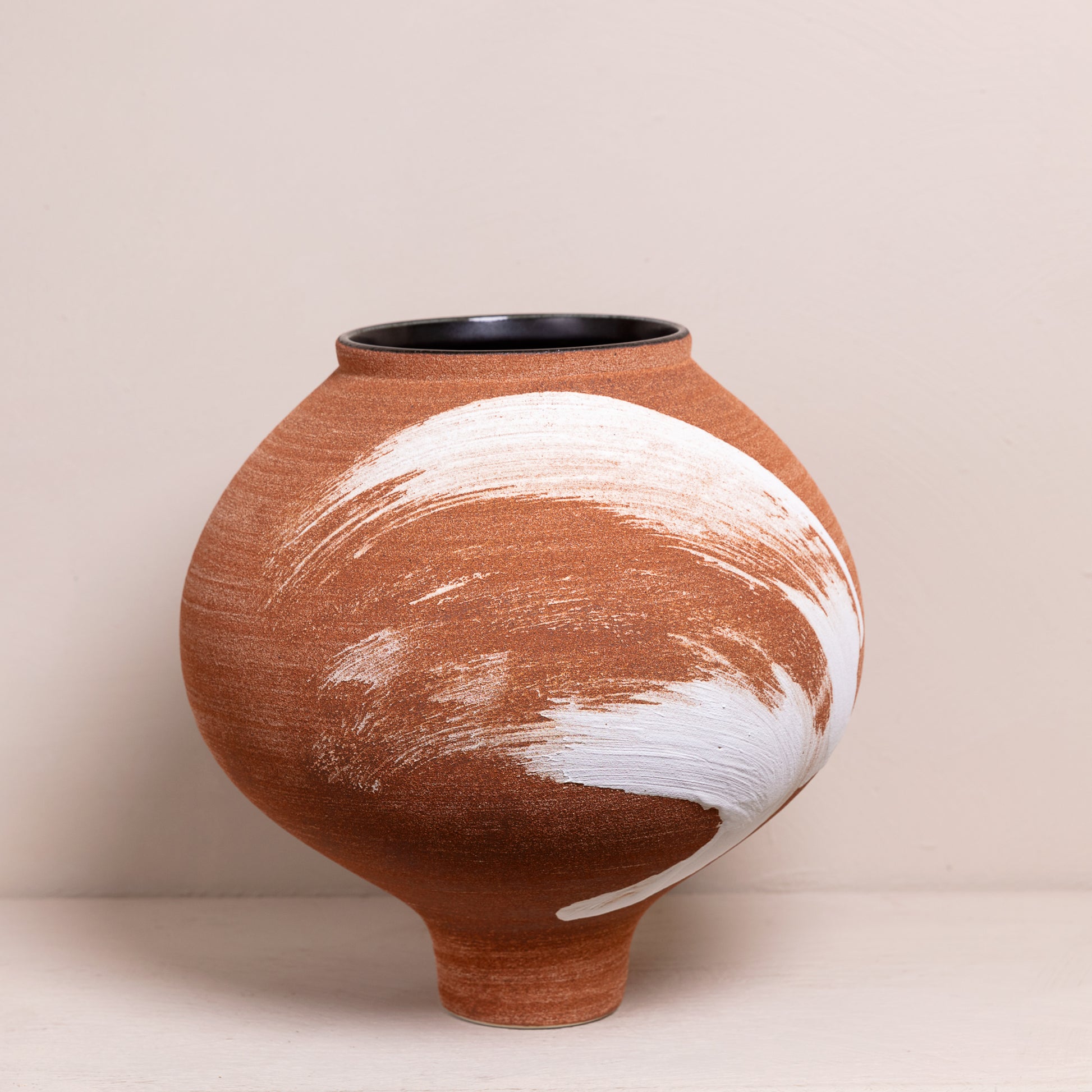 Handgemaakte aardewerk vaas met unieke witte penseelstreek op een terracotta basis, modern en rustiek ontwerp.